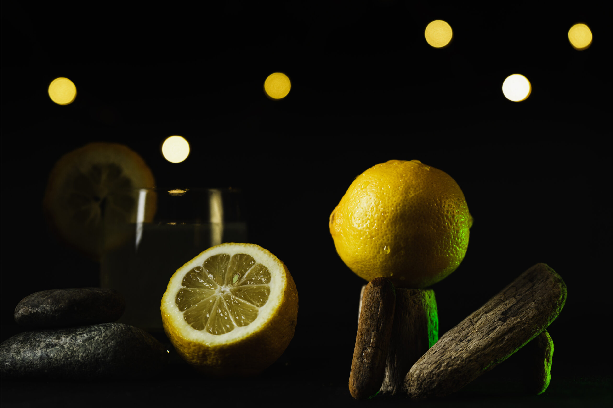 présentation de citron avec citronnade sur fond noir, lumière verte et décoration organique.